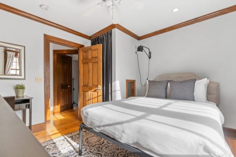 Cozy bedroom with a white bed, grey pillows, wooden accents, and natural light.