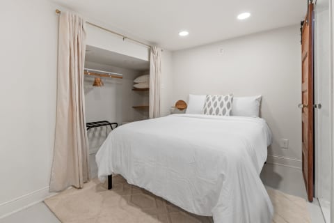 A cozy bedroom featuring a white bed, beige curtains, and a wooden door.