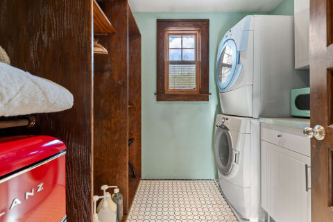 A laundry room featuring a stacked washer and dryer, wooden shelves, and a red refrigerator.