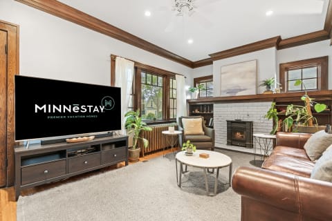 Cozy living room with a leather sofa, wooden accents, and a modern television displaying 'MINNēSTAY' logo.