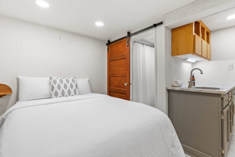 A modern bedroom with a bed, wooden sliding door, and a small kitchenette area.