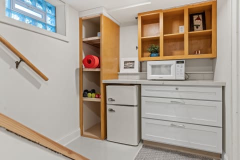 A basement kitchenette featuring a microwave, refrigerator, and fitness gear like weights and yoga mats.