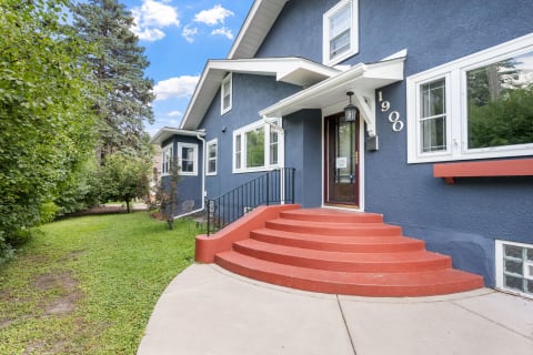 A blue house with red steps leading to the front door, surrounded by greenery and bright blue sky.