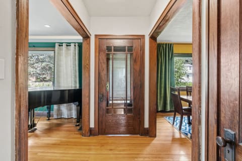 A cozy entryway showing a wooden door, grand piano, and dining area with green curtains.