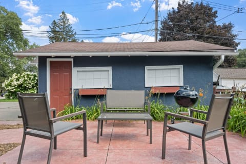 Outdoor seating in front of a blue building with a red door and grill.