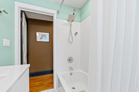 Modern bathroom featuring a mint green wall, a white bathtub, and a shower area with a curtain.