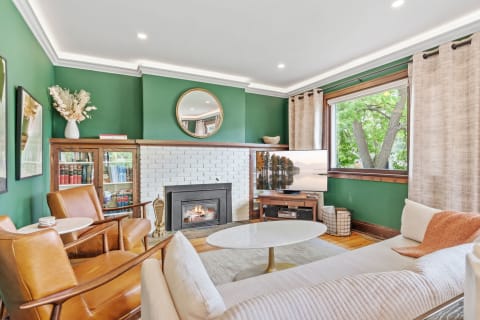A stylish living room with green walls, a white brick fireplace, and vintage leather armchairs.
