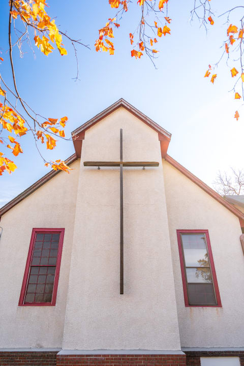 Church facade with a wooden cross and autumn leaves.