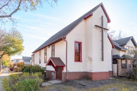 Side view of a church featuring a wooden cross and red-trimmed windows.