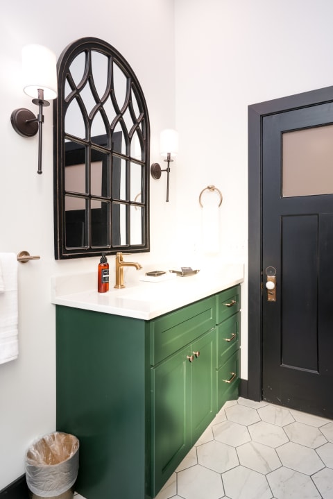 Modern bathroom featuring deep green cabinetry, a Gothic-style mirror, and brass fixtures.