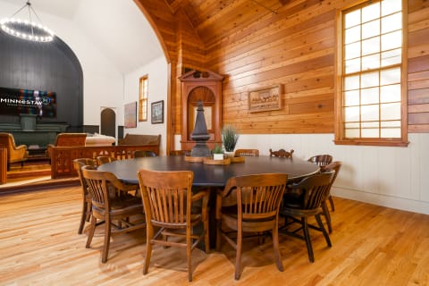 A room featuring a round table surrounded by wooden chairs, wooden walls, and a cozy sitting area.