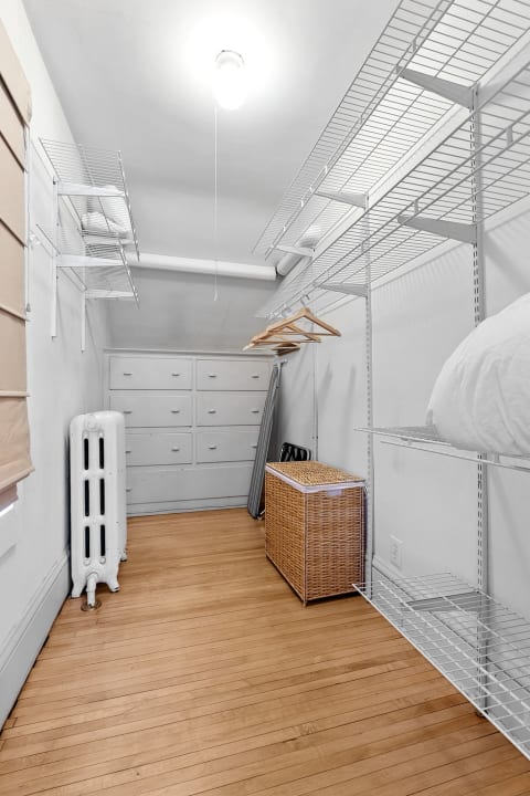 A spacious closet with white walls, wire shelves, a wicker basket, and polished wooden flooring.