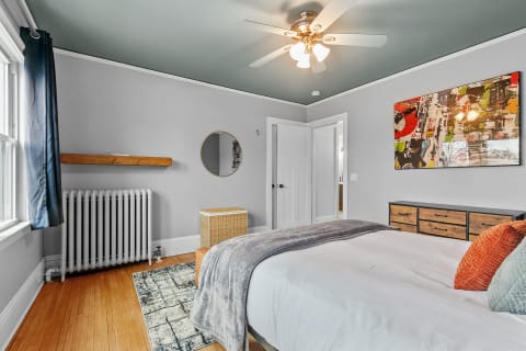 A well-decorated bedroom featuring a bed, wooden dresser, and artistic accents.