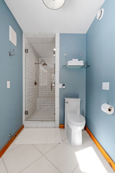 Modern bathroom with blue walls, shower, toilet, and white towels.