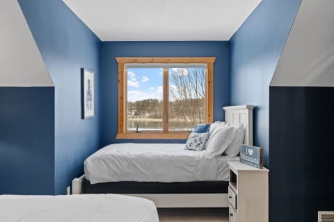 A cozy bedroom with blue walls and a large window overlooking a natural scene.
