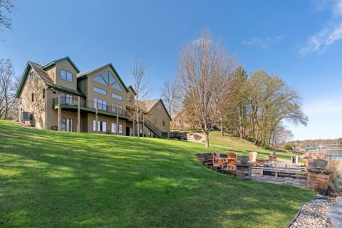 Lakeside house with green lawn and patio area overlooking the water.