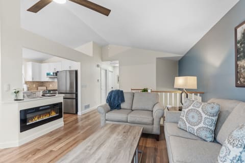 A stylish living room featuring a gray sofa, wooden coffee table, and an open kitchen in the background.