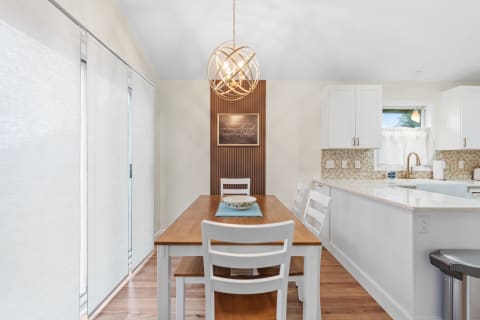 A cozy dining area with a wooden table, white chairs, decorative lighting, and kitchen views.