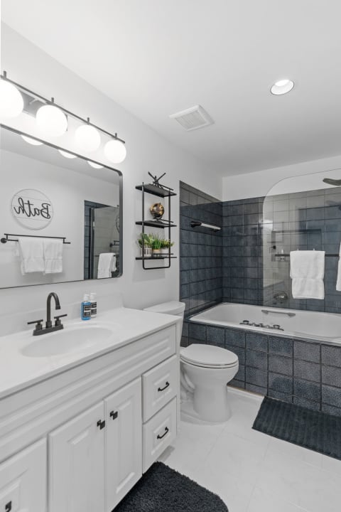 A bright and clean bathroom featuring a dual sink vanity, dark tiles, and a soaking tub.