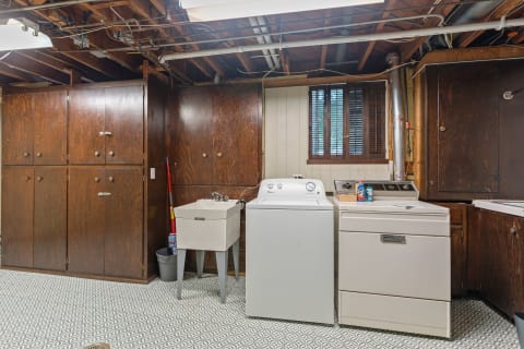 Laundry area in a basement featuring a washing machine, dryer, and utility sink among wooden cabinets.