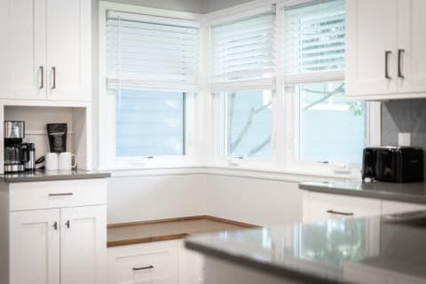 Bright kitchen with white cabinets, coffee maker, and natural light from windows.