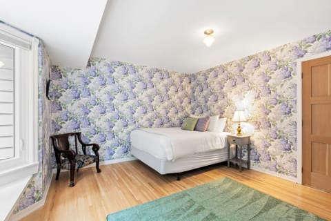 Bedroom featuring floral wallpaper, a white bed, and a wooden chair.