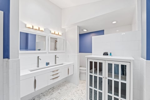 Modern bathroom with white cabinetry, twin sinks, blue accent wall, and stylish fixtures.