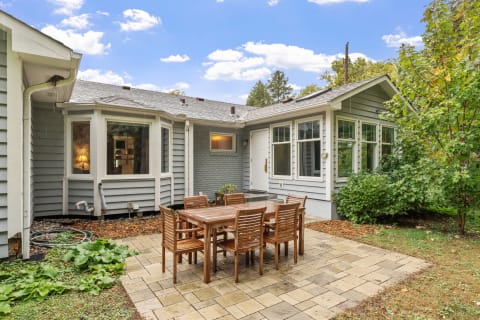 Outdoor patio with wooden table and chairs near a light gray house.