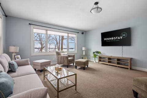 A bright living room featuring a sofa, armchair, and large windows overlooking nature.