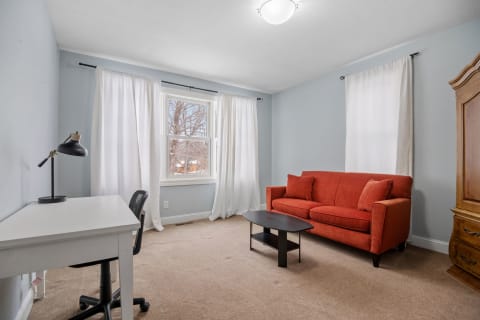 A bright room with blue walls, an orange couch, a white desk, and a decorative wooden cabinet.