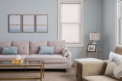 A light pink sofa with aqua pillows in a living room, alongside abstract wall art and a cozy armchair.