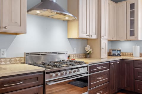 A modern kitchen featuring a stainless steel gas range, hood vent, and a combination of light and dark wood cabinetry.