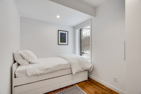 Minimalist bedroom featuring a single bed, large window with snowy scenery, and abstract wall art.