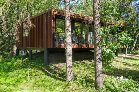 Modern cabin with wooden slats on stilts in a green landscape.