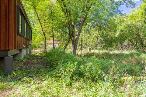 A wooden building next to a patch of greenery and trees under a clear sky.