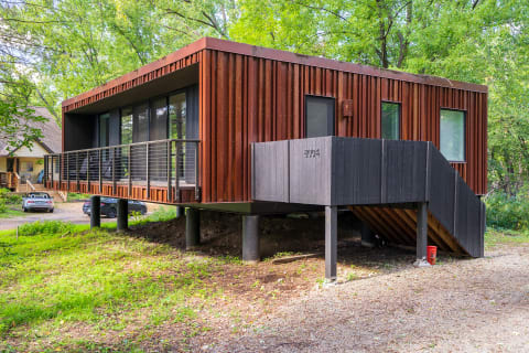 Contemporary elevated house with wooden slats and large windows, set in a lush green environment.
