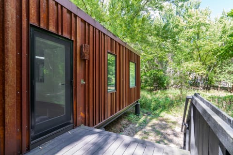 A modern house with rust-colored corrugated metal exterior and large windows surrounded by greenery.