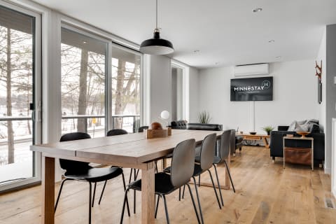Modern dining area with a wooden table, black chairs, and large windows overlooking a snowy landscape.
