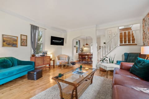 Cozy living room featuring teal and brown sofas, a glass coffee table, and a dining area in the background.