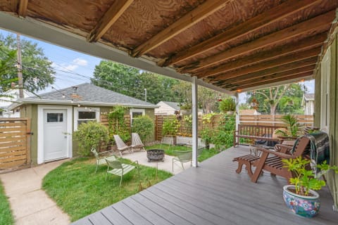 Outdoor patio with seating and garden, featuring a fire pit and greenery.
