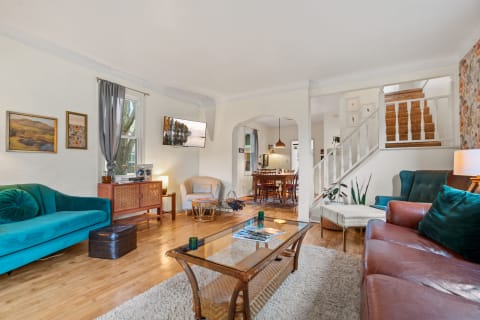 A stylish living room with teal and brown sofas, a glass coffee table, and a dining area in the background.