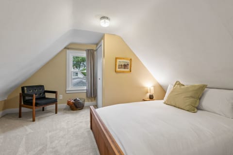 Cozy attic bedroom featuring a bed, armchair, and a window.