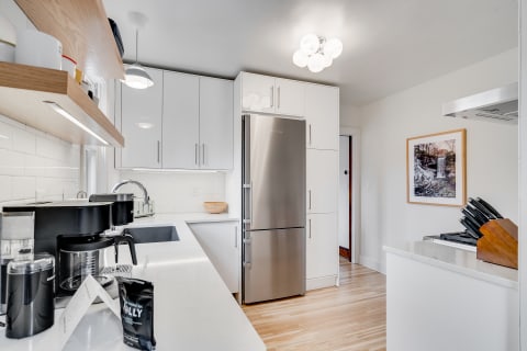 A contemporary kitchen with white cabinets, stainless steel refrigerator, and a coffee maker on the counter.