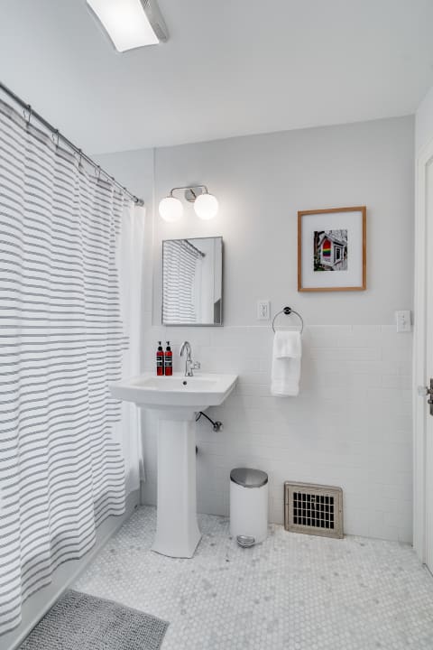 Modern bathroom with a marble floor, pedestal sink, and striped shower curtain.
