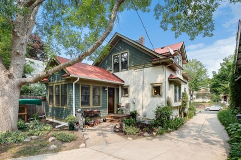 Charming two-story house with green siding and red roof surrounded by lush garden.