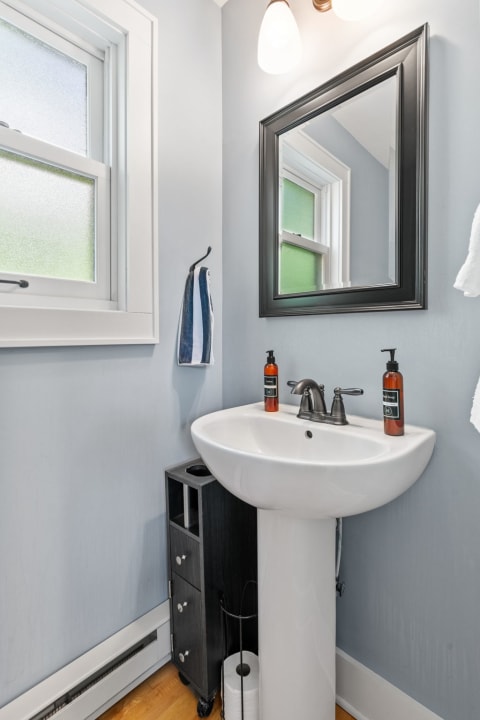 Modern bathroom featuring a pedestal sink, amber soap bottles, and a stylish mirror.