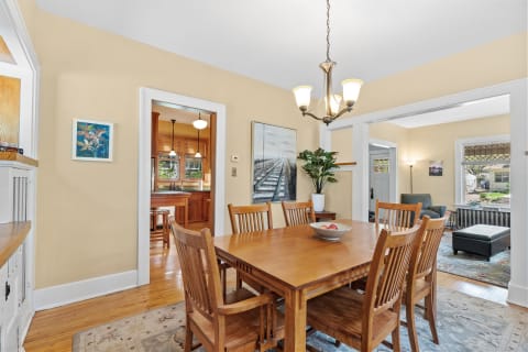 Dining room featuring a wooden table, chairs, a chandelier, and a view of a kitchen.