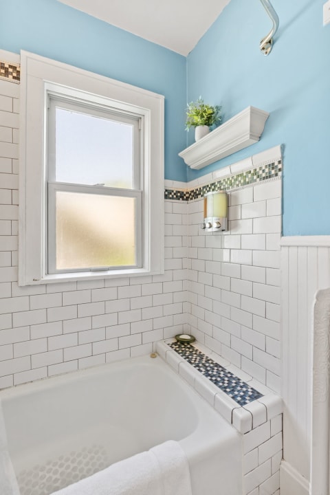 A bathroom corner featuring a white bathtub, blue walls, and a decorative tile border.