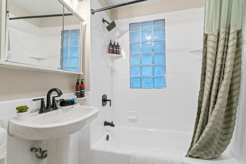 A clean and modern bathroom featuring a white pedestal sink, bathtub, and a green shower curtain.