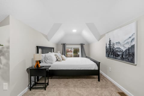 A cozy bedroom with a sloped ceiling, a bed, nightstand, and mountain-themed artwork.